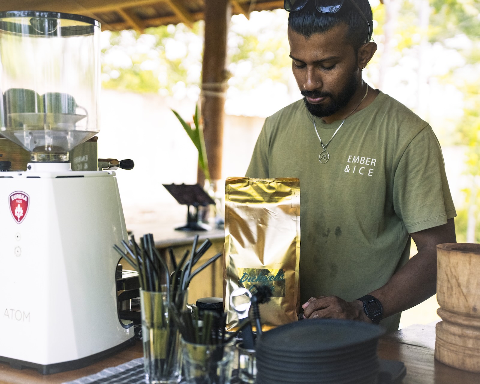 Barista in an Ember & Ice tee opening a bag of beans behind the espresso machine