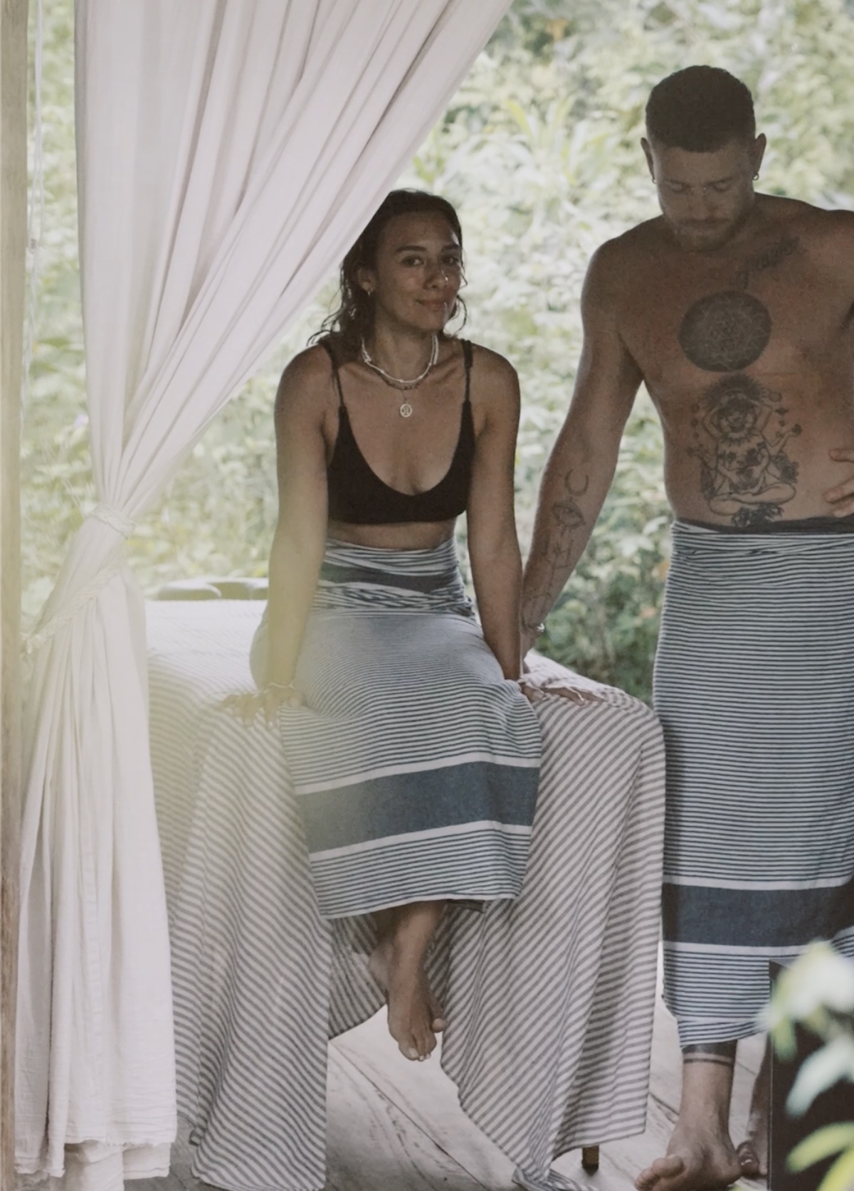 The open-air treatment room — two therapists in sarongs by the linen-draped table, jungle behind
