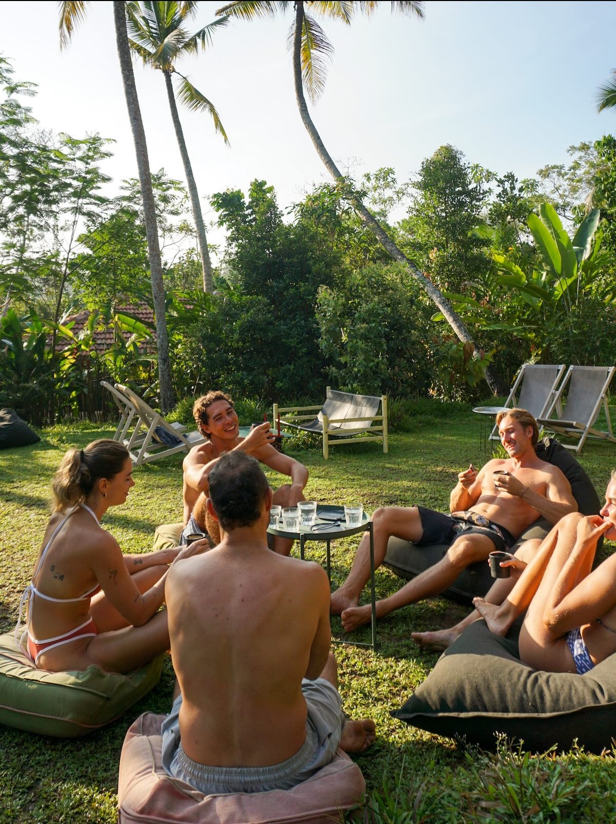 Friends lounging on beanbags in the garden with coffees, palms overhead